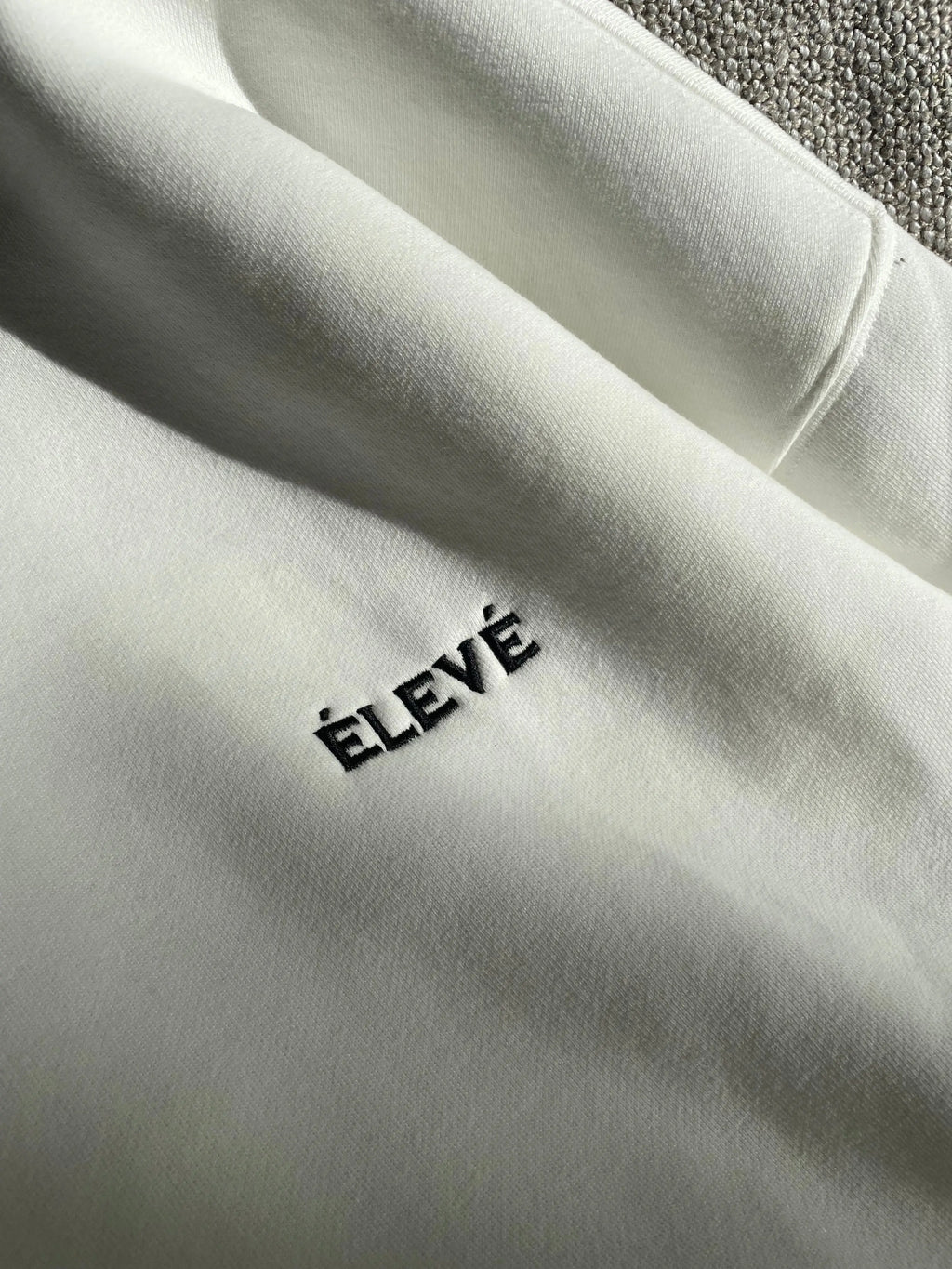 Detailaufnahme ÉLEVÉ Logo Stickerei auf weißem Prestige Hoodie – hochwertiger Heavyweight Streetwear Stoff